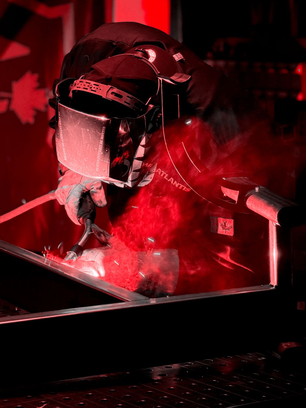 An Atlantis welder joins a steel frame in the Laval factory, a Canadian flag behind him